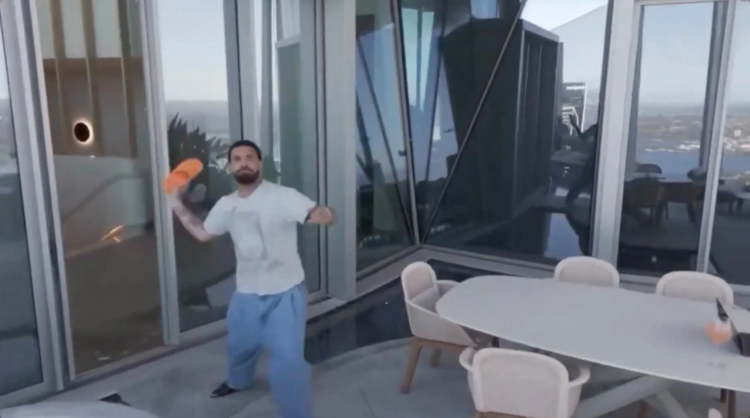 A man in white T-shirt and jeans poised to throw a bright orange slider at something in the air on his patio