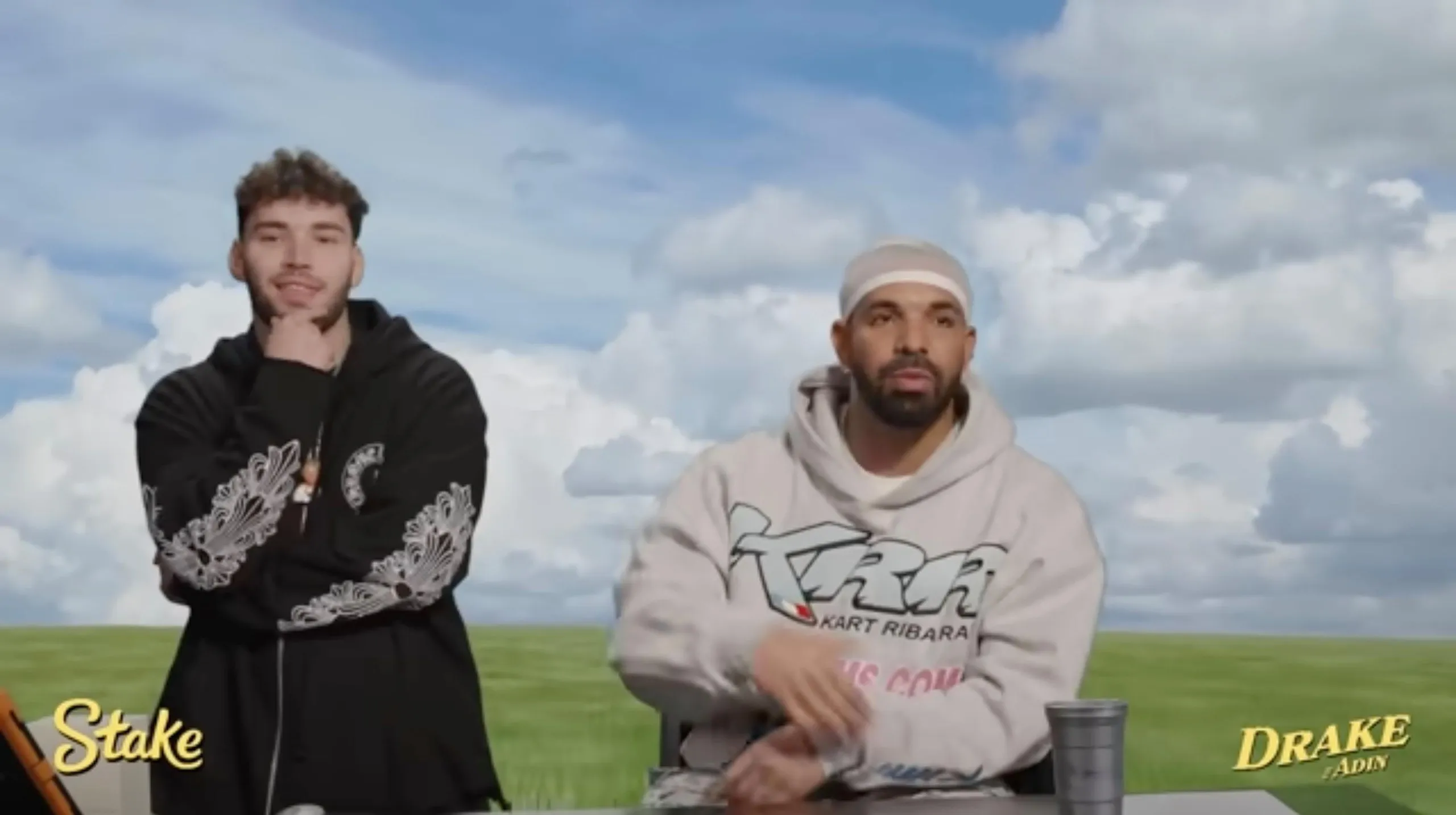 Two men in hooded sweatshirts standing in front of a studio shot of a field 