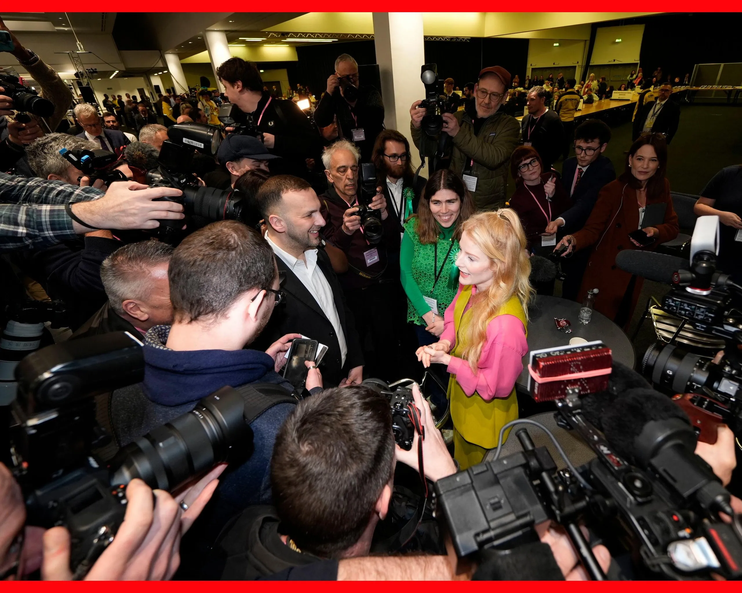 A smiling Spencer is surrounded by people with cameras 
