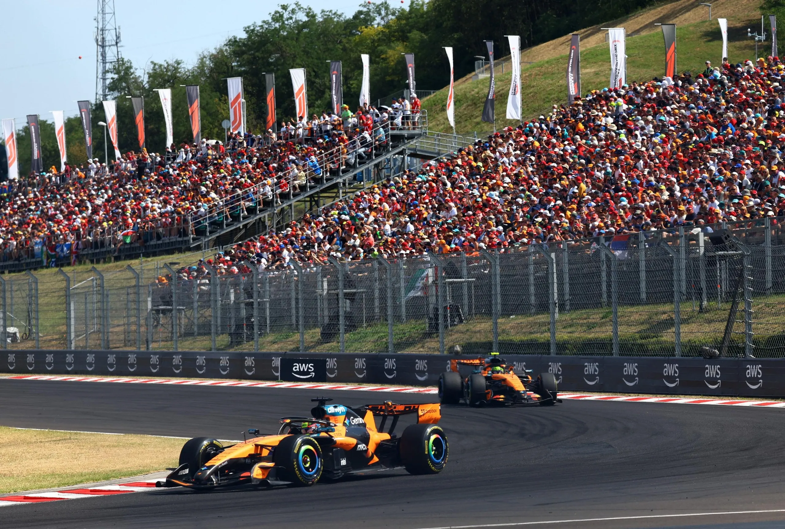 Oscar Piastri driving ahead of Lando Norris in front of a stand full of spectators.