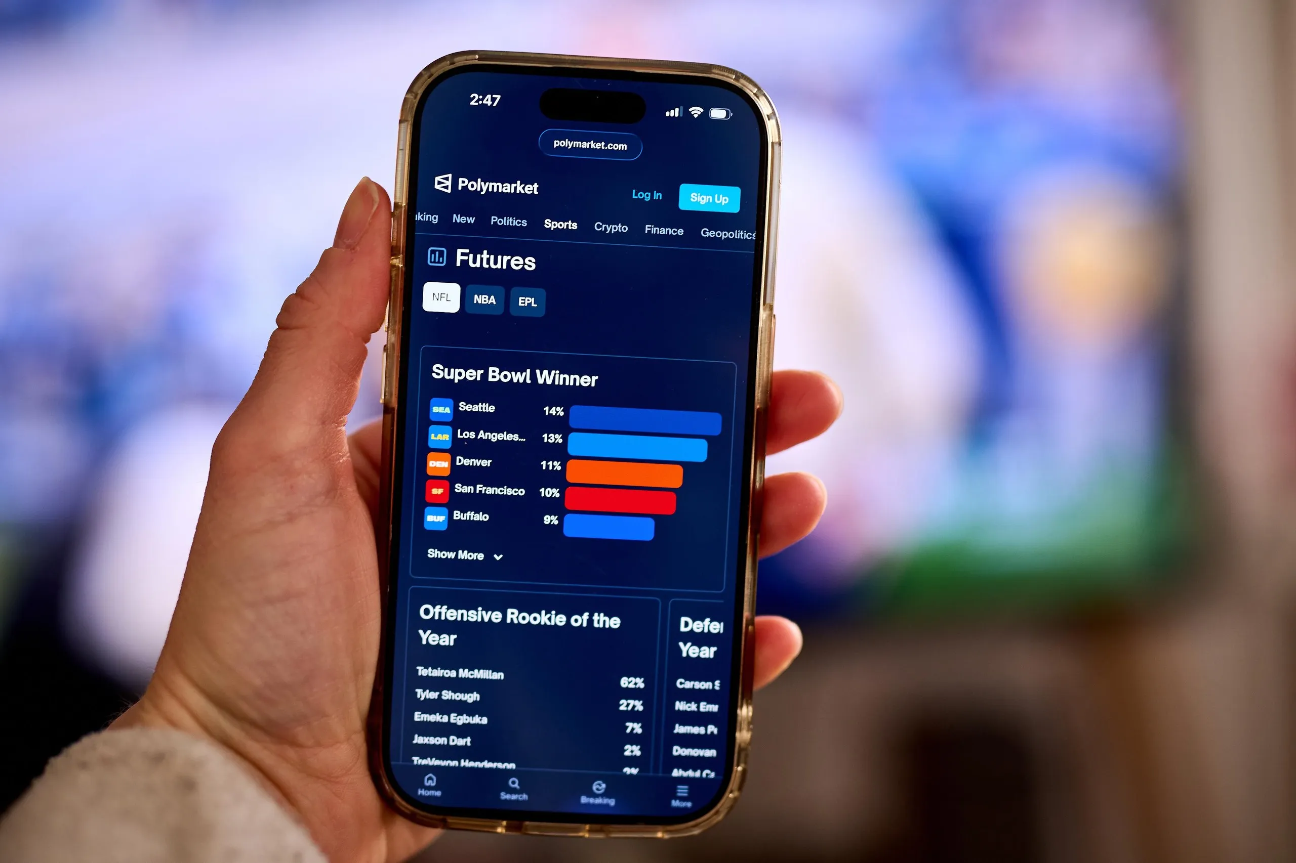 A hand holds a phone displaying the Polymarket app