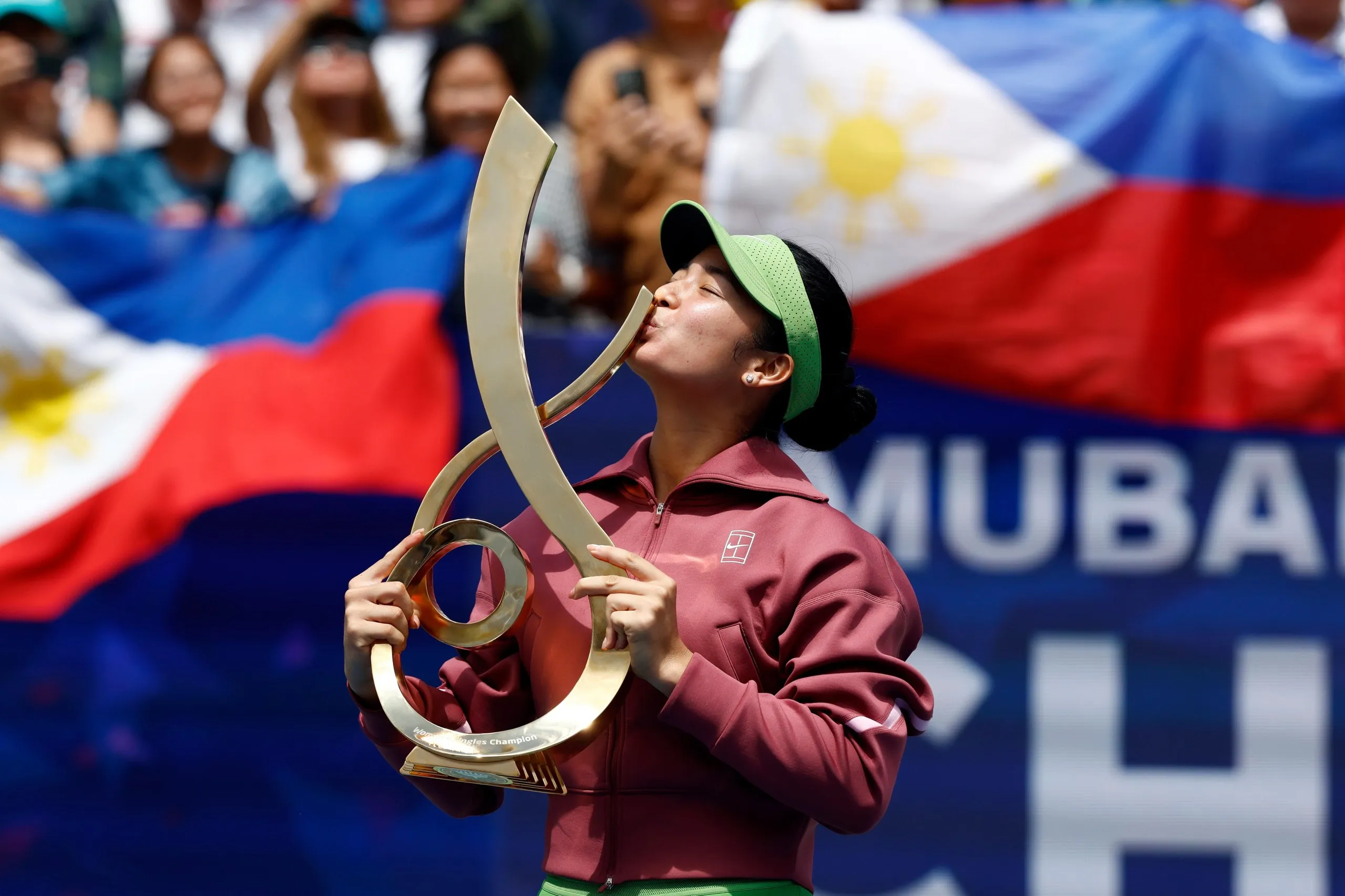 Alexandra Eala celebrates with the DC Open trophy as fans fly the Filipino flag behind her.