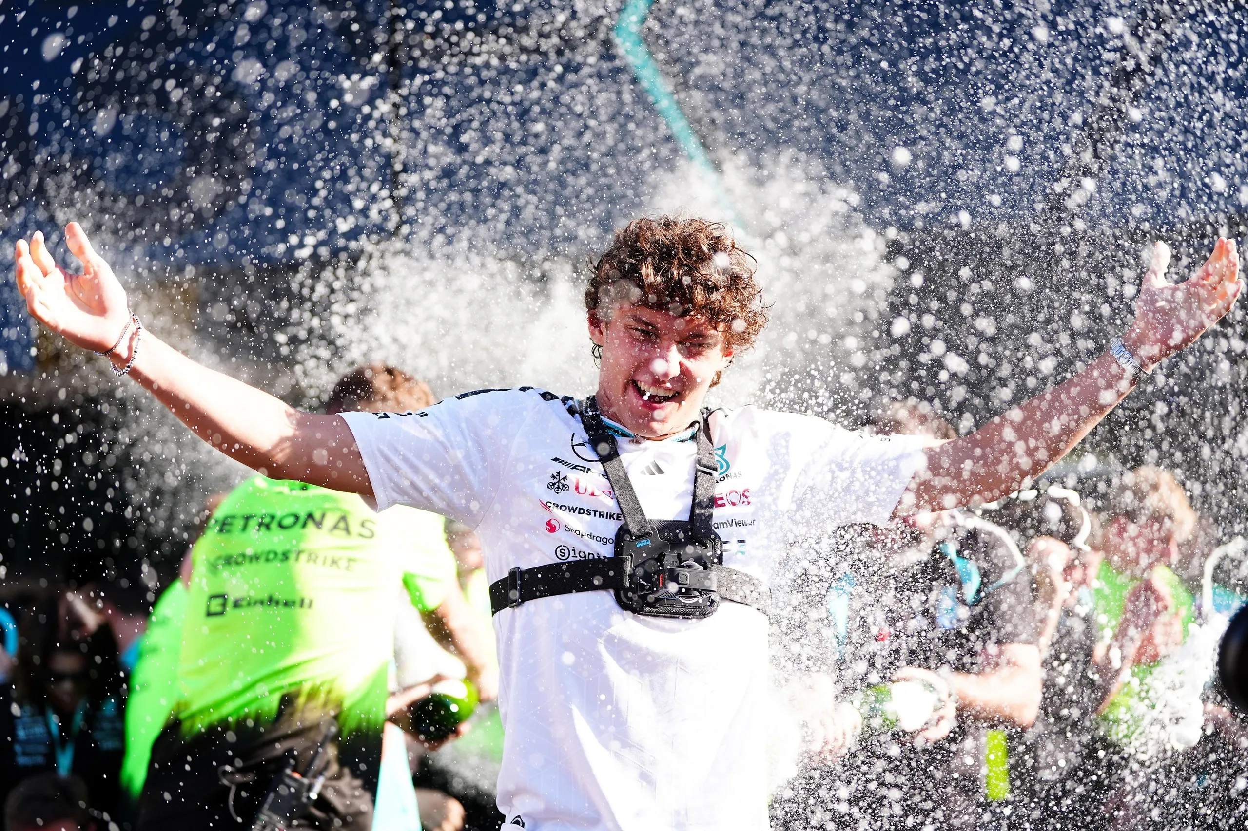 Kimi Antonelli, wearing a white T-shirt and with his hands outstretched, is sprayed after winning the Spanish Grand Prix